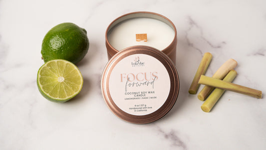 A rose gold candle tin with sprigs of fresh lemongrass on the right side and slices of lime on the left side.